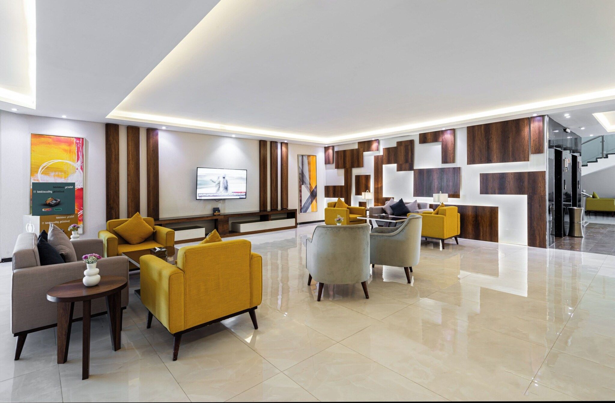 A modern lobby with a flat-screen TV, multiple seating areas, and a staircase.
