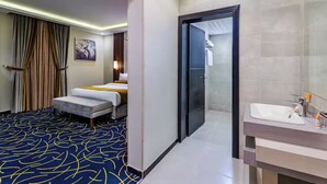 Quarto de hotel com cama, banheiro com pia e porta que dá para outro cômodo.