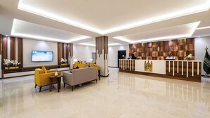 Um saguão moderno de hotel com balcão de recepção, área de estar e uma tela de televisão.