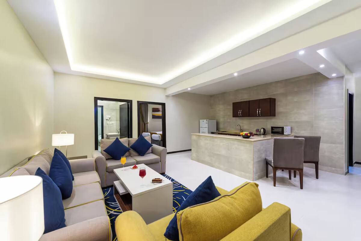 A modern living room with a sofa, coffee table, and a small kitchen area with a microwave and cabinets.