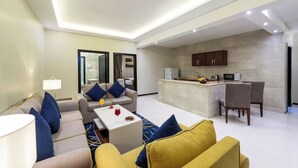 Sala moderna com sofá, mesa de centro e pequena cozinha equipada com micro-ondas e armários.