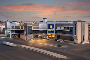 A modern hotel with a prominent sign, multiple floors, and a parking area.