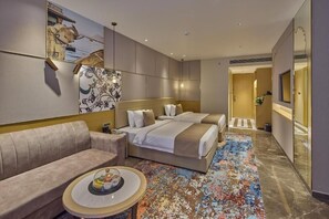 Habitació d'hotel amb un sofà, dos llits, una catifa colorida i un mirall gran.