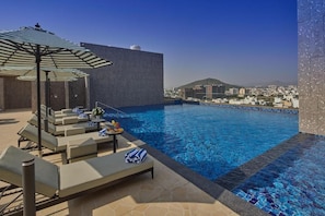 A rooftop pool with lounge chairs and umbrellas, a clear view of the cityscape, and a tiled pool edge. - Grand Continent Luxury Collection, Udaipur (Udaipur)