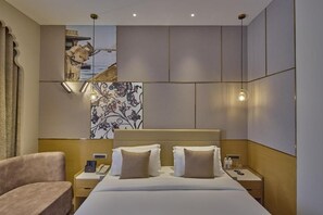 A hotel room with a bed, bedside tables, a chair, artwork, and a view of the sea. - Grand Continent Luxury Collection, Udaipur (Udaipur)