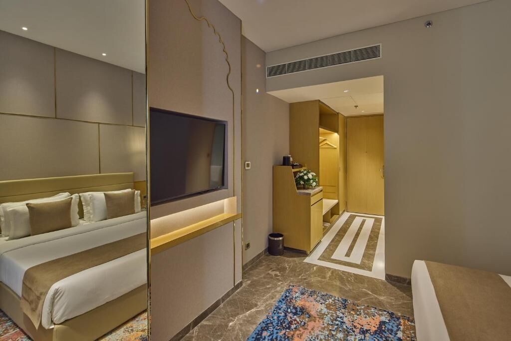 Habitación de hotel con cama, televisión, escritorio y baño visible a través de una puerta abierta.