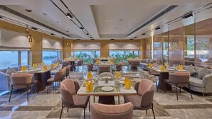 A spacious dining area with multiple tables and chairs, large windows, and a view of the outdoors. - Grand Continent Luxury Collection, Udaipur (Udaipur)