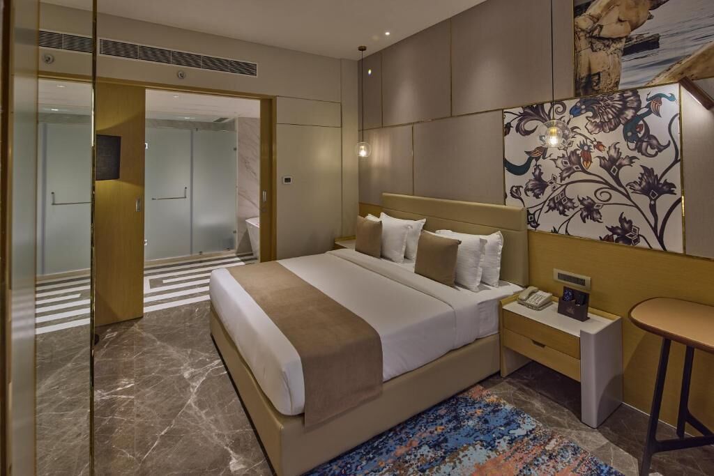 Una habitación de hotel moderna con una cama grande, mesitas de noche, un escritorio pequeño y un papel tapiz con estampado.