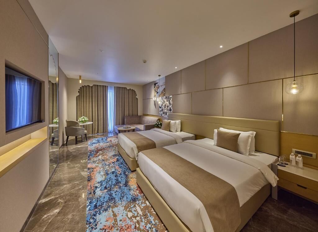 Una habitación de hotel con dos camas, un escritorio, una silla, un televisor y un ventanal con cortinas.