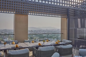 A rooftop dining area with tables and chairs, a view of the cityscape, and a metal fence. - Grand Continent Luxury Collection, Udaipur (Udaipur)