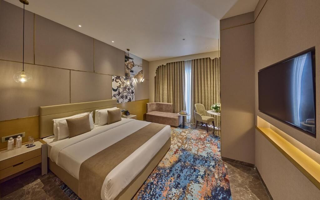 Habitación de hotel con una cama grande, un escritorio, una silla, un televisor y una ventana con cortinas.