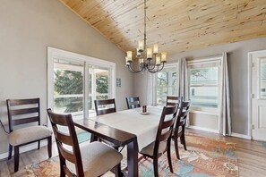 Une salle à manger avec un plafond en bois, de grandes fenêtres et un lustre.