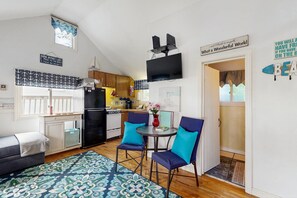 A compact living space with a kitchenette, a dining area with two chairs, a sofa, and a patterned rug.