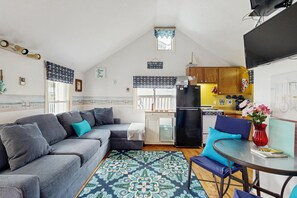 A compact living space with a sofa, a dining table, a kitchen area, and a small window with curtains.