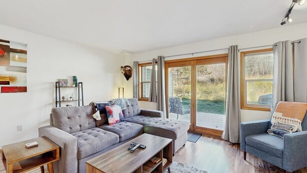 A modern living room with a sectional sofa, a coffee table, a side table, a blue armchair, and a large window with curtains. - Stylish townhouse with WiFi, private washer/dryer, patio, and full kitchen (Big Sky)