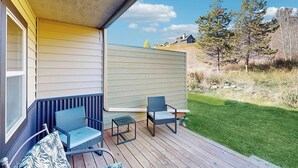 A covered outdoor area with two chairs and a small table, a grassy lawn, and a view of trees and hills. - Stylish townhouse with WiFi, private washer/dryer, patio, and full kitchen (Big Sky)