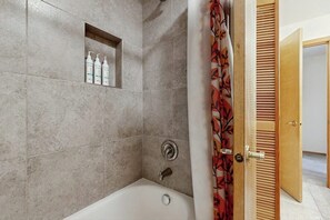 Een badkamer met een douche, een bad en een plank met toiletartikelen.