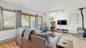 A modern living room with a sofa, TV, fireplace, and large windows. - Stylish townhouse with WiFi, private washer/dryer, patio, and full kitchen (Big Sky)