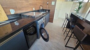 Une cuisine compacte équipée d’un lave-linge, d’un évier et d’un coin bar avec des tabourets.