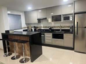 Eine moderne Küche mit Edelstahlgeräten, einer Kücheninsel mit schwarzer Arbeitsplatte und Barhocker sowie einer gefliesten Spritzschutzwand.