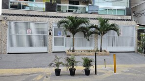 Un immeuble fermé par un portail, une petite jardinière avec des palmiers et un poteau jaune.
