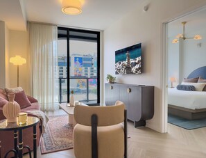 Ein modernes Hotelzimmer mit einer Couch, einem Sessel, einem kleinen Tisch, einem Schrank, einem Bett und einem großen Fenster mit Blick auf die Stadt.