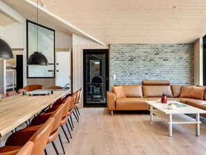 A modern living room with a wooden dining table, leather sofas, and a brick wall. - 5 Star Holiday Home in Hjorring (Hjørring)