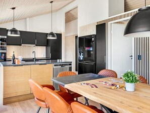 A modern kitchen with black cabinets, a wooden island, and a dining area with orange chairs and a table. - 5 Star Holiday Home in Hjorring (Hjørring)