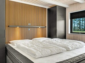 A modern bedroom with a bed, wooden panel wall, and a window with a view of trees. - 5 Star Holiday Home in Hjorring (Hjørring)