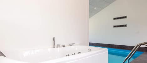 Un baño moderno con una bañera blanca grande, una zona de ducha separada y una piscina.