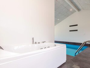 A modern bathroom with a large white bathtub, a separate shower area, and a pool. - 5 Star Holiday Home in Hjorring (Hjørring)
