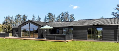 Una casa moderna de dos pisos con una terraza grande, un área de estar cubierta al aire libre y vistas del bosque circundante.