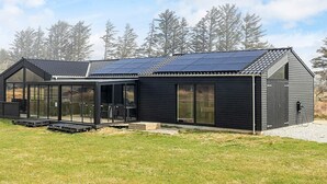 Une maison moderne dotée d’un toit recouvert de panneaux solaires, de grandes fenêtres et d’un patio abrité.