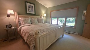 Une chambre à coucher avec un lit, des lampes de chevet, un tableau encadré au mur et une fenêtre avec des stores.