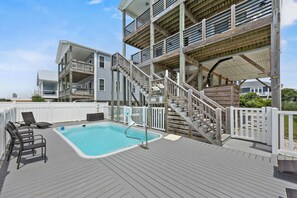 Ein Poolbereich mit Holzterrasse, Schwimmbecken und einer Treppe zu einem mehrstöckigen Gebäude.
