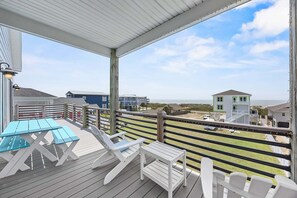 Una terraza techada al aire libre con una mesa y sillas, con vistas a una playa y edificios.