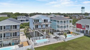 Un área residencial costera con varias casas de dos pisos, balcones, una piscina y un tanque de agua al fondo.