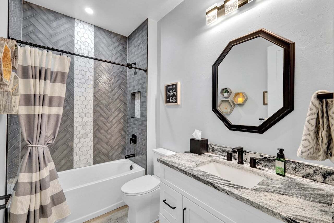 Un bagno moderno con pannelli a mosaico a motivi a spina di pesce, uno specchio grande e una tenda da doccia.