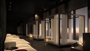 A modern hotel room with a long row of beds, a small table, and a view of the city at sunset. - Roomers Parkview, A Luxury Collection Hotel, Frankfurt (Frankfurt)