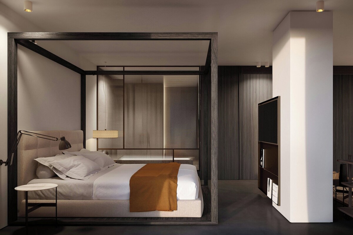 Ein modernes Hotelzimmer mit Bett, Nachttisch, Lampe und einem großen Fenster.