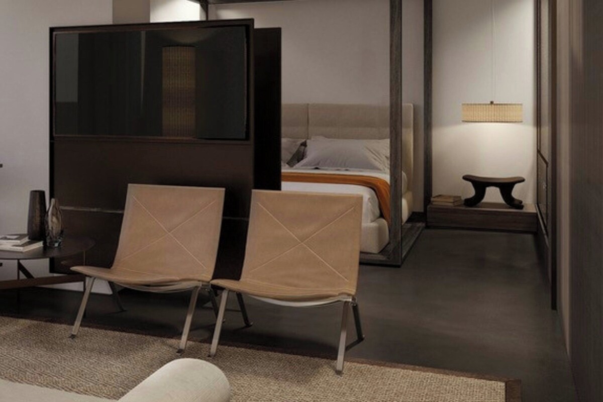 Ein Hotelzimmer mit Bett, Schreibtisch, zwei Stühlen, Fernseher und einem kleinen Tisch mit Lampe.