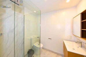 Un baño moderno con ducha envuelta en vidrio, inodoro blanco y tocador con espejo.
