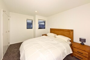 Un dormitorio con cama, mesita de noche, lámpara y dos ventanas.