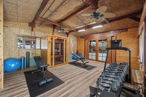 Une salle de sport équipée de matériel d’exercice, avec des murs en bois et un ventilateur au plafond.