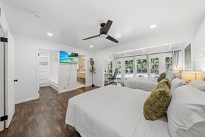 Une chambre à coucher avec un lit, un ventilateur de plafond, un bureau et une vue sur l’extérieur.