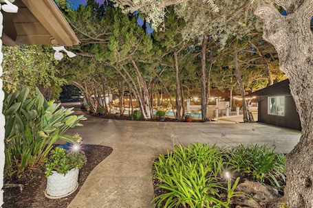 A landscaped outdoor area with a pathway, trees, and a building with large windows.. 4 BR - 2 Bath, Sauna, Gym, Pool, 7 Bed, Parking Yard, Ranch Style