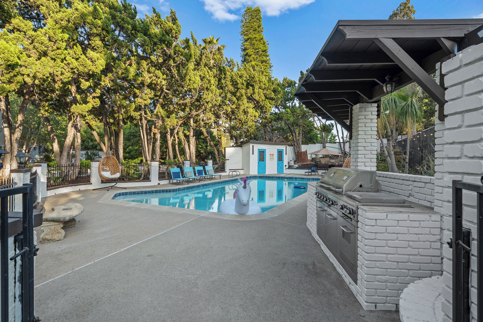 A swimming pool with a stone border, a barbecue area, and a covered seating area.