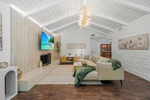 A spacious living room with a high ceiling, a large flat-screen TV, a sofa, and a fireplace.