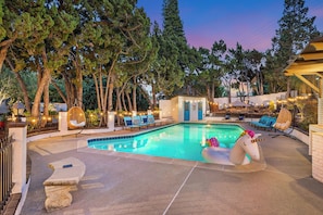 A swimming pool with lounge chairs, a small building, and trees.