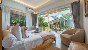 A modern bedroom with a large bed, a sofa, and a dining area with a view of the garden.